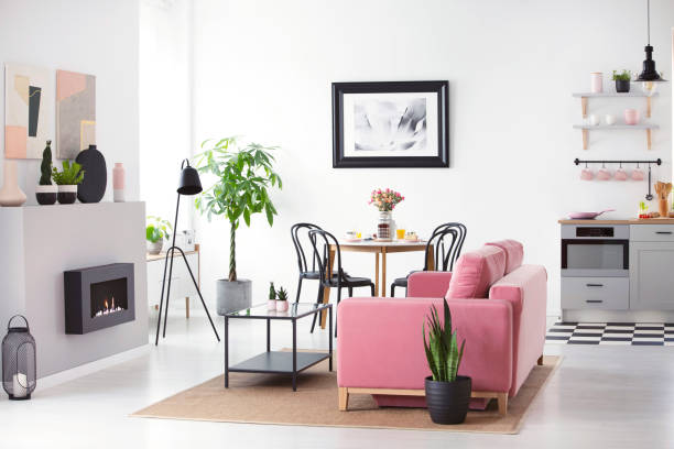 istock Kitchenette in open space interior with poster above table and plant next to pink sofa. Real photo 1007737098