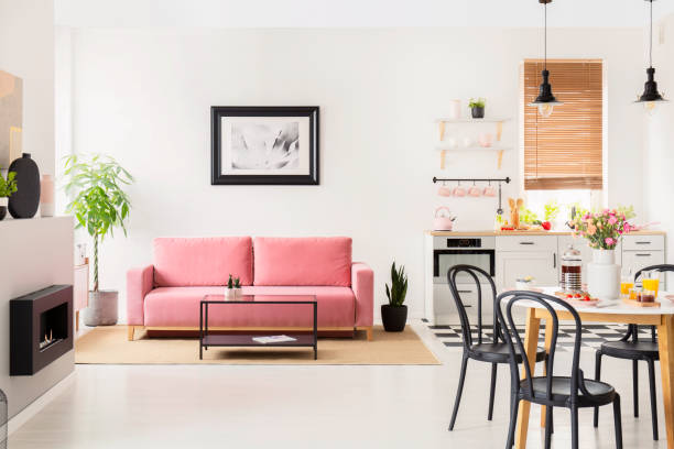 istock Black chairs at dining table in white flat interior with kitchenette and posters above couch. Real photo 1007737112