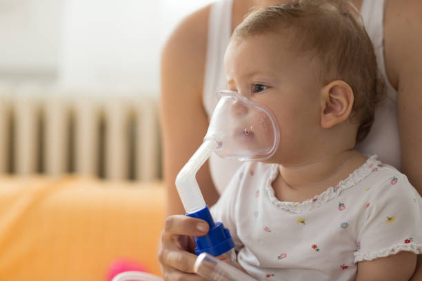 Baby taking respiratory inhalation therapy. Mother holding the mask of a nebuliser Baby taking respiratory inhalation therapy. Mother holding the mask of a nebuliser bronchitis stock pictures, royalty-free photos & images