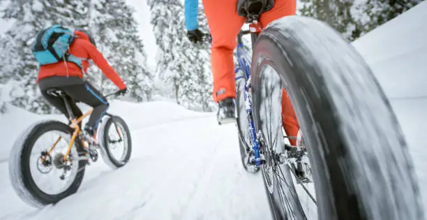 Rear view of male and female mountain bikers riding fatbikes on snow covered landscape.