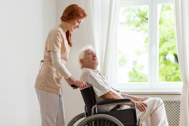 istock Smiling nurse supporting disabled senior man in the wheelchair 1007763648