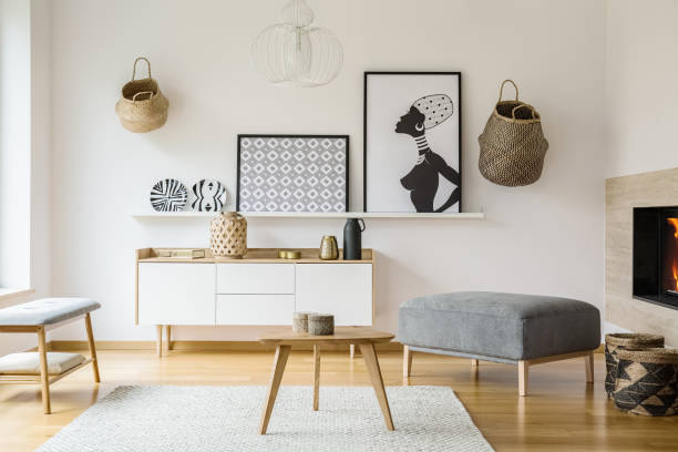istock Posters and baskets on white wall in bright flat interior with wooden table next to pouf. Real photo 1007769262