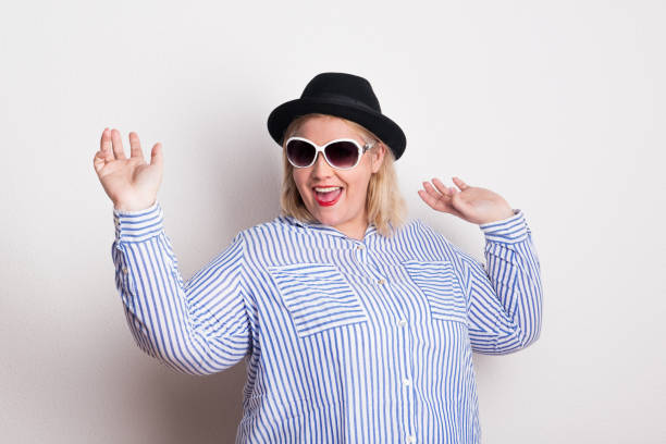 Portrait of an attractive overweight woman with hat and sunglasses in studio. Portrait of an attractive overweight woman with black hat and sunglasses in studio on a white background. big fat lips stock pictures, royalty-free photos & images
