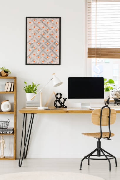 istock Poster on white wall above wooden desk with lamp and desktop computer in workspace interior. Real photo 1007785314