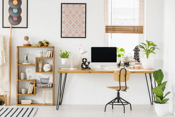 istock Large industrial desk with a computer by a window, a wooden bookcase and posters on a white wall in a stylish, scandi home office interior 1007785346
