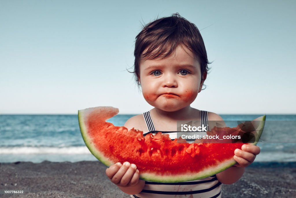is it delicious?! funny little girl on the beach eating watermelon and making funny face. Child Stock Photo