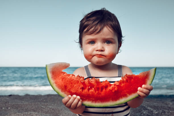 is it delicious?! funny little girl on the beach eating watermelon and making funny face. children at the beach stock pictures, royalty-free photos & images