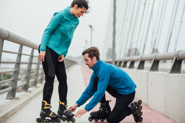 istock Young man kneeling and fixing girlfriend's roller skates 1007786720