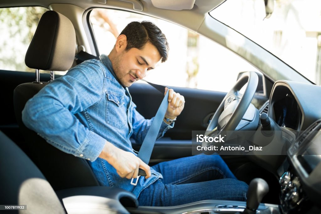 Man fastening seat belt in the car Young latin man sitting on car seat fastening seat belt Seat Belt Stock Photo