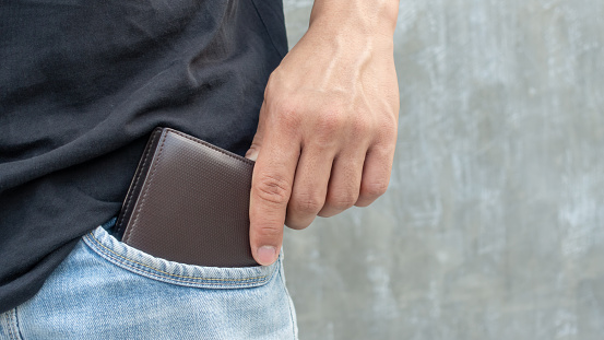 Men hold a brown wallet from a jeans pocket.