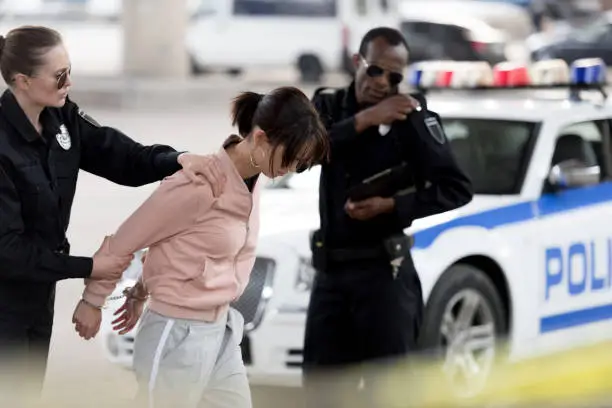 Photo of policewoman holding arrested young woman while her partner talking on portable radio
