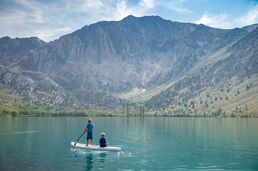 Brothers on a Paddle Boarding On An Alpine Lake.  The boy is fishing off the back of the board.