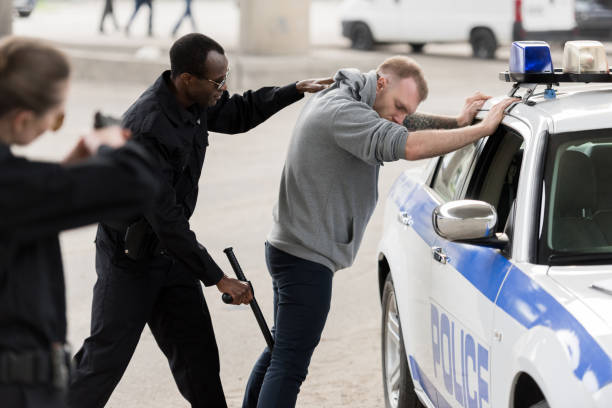 вид сбоку афро-американец арест человека в то время как женщина-полицейский, направленных на него пистолетом - weapon gun order handgun стоковые фото и изображения