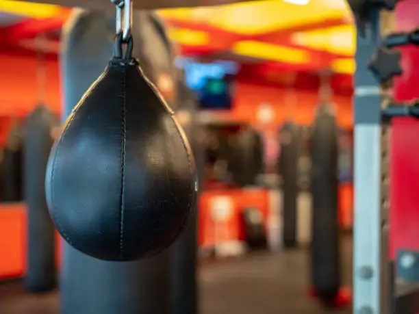 A black leather speedbag, with Muay Thai bags in the back, ready for use in a gym