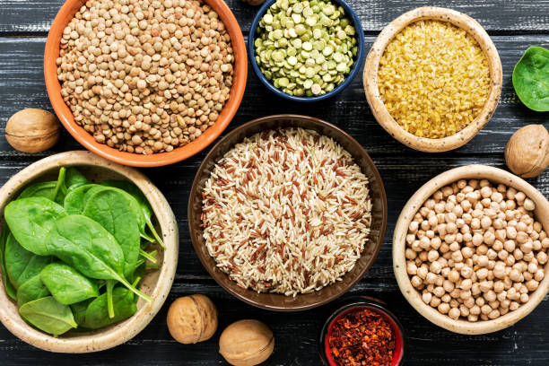 Chickpeas, lentils, peas, brown rice, bulgur, nuts and spinach on black rustic background. Various cereals and legumes. Vegetarian food. View from above