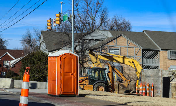 salle de bain portatif au chantier de construction à intersectio de routes urbaines avec la pelleteuse dans un cône de fond et de la circulation autour de - porta potty photos et images de collection