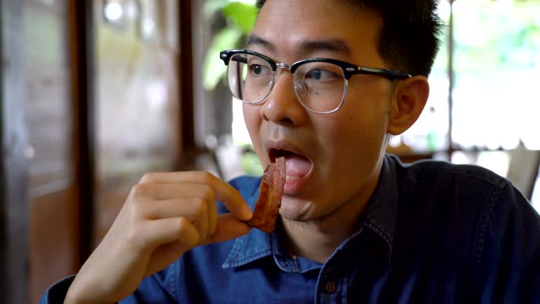 Asian Man Eating Bacon in Restaurant