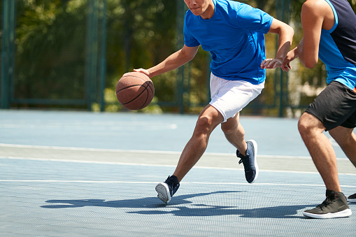 young asian male basketball player playing one-on-one on outdoor court.