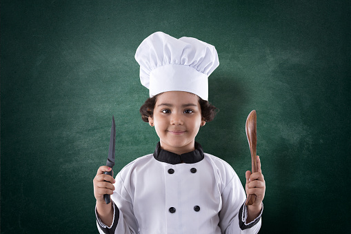 Little girl chef holding spatula and kitchen knife