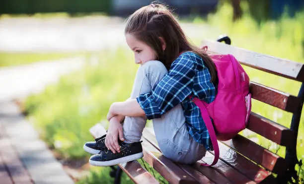 Photo of Unhappy schoolgirl sitting in the park. Education, lifestyle concept