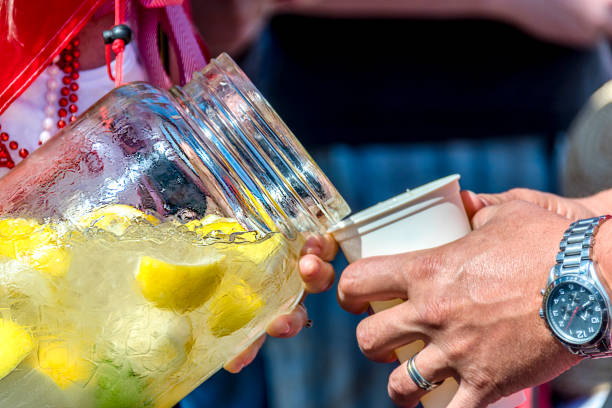Woman in beads pours cold water with ice and carved lemons from a glass bottle