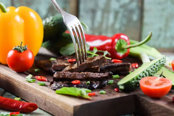 Paleo diet. Healthy nutritious protein meal. Homemade well done steak on oak board served with tomatoes, cucumbers and chili pepper closeup