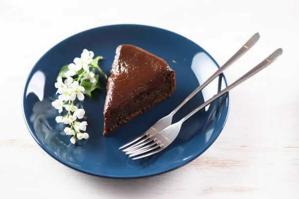 Healthy traditional Siberian dessert. Bird cherry cake with chocolate ganache served with white bird cherry flowers in navy blue plate with thin forks on white table