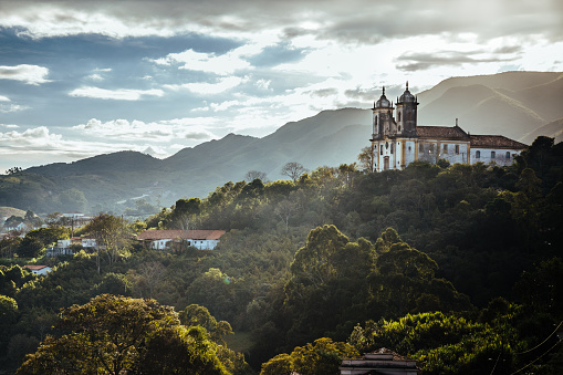 Paisaje de ciudad de Ouro Preto de Minas Gerais, Brasil con la iglesia de Sao Francisco de Paula en la cima de una montaña bajo el sol y las nubes oscuras. photo
