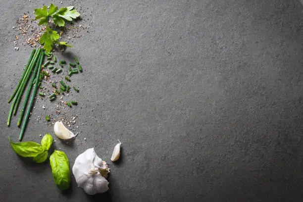 Photo of Top Down View On Kitchen Ingredients Like Garlic, Basil, Spices And Herbs On Slate Stone, With Free Space In The Middle And Right Side