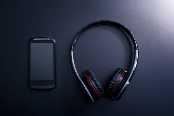 istock Black Mobile Phone Lying Next A Black Overhead Headset On Dark Background With Reflection 1008052378