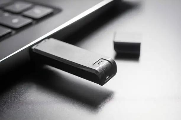 A Macro Of A Black USB Memory Stick Plugged Into The USB Port Of A Black Laptop, Side View