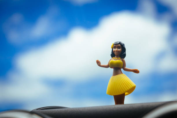 istock Hawaiian hula dancer doll dancing over the front panel of a car, with blue sky with some clouds on the road. 1008056914