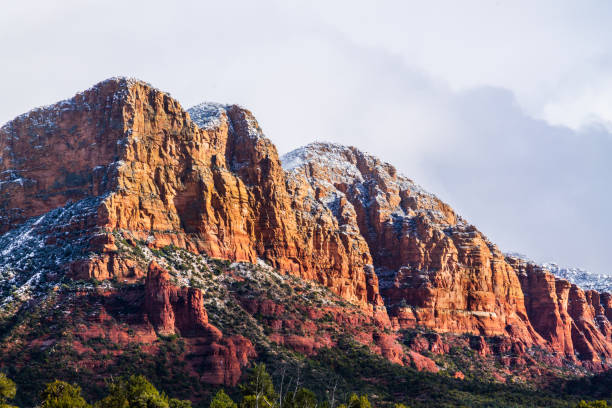 istock Red rocky hill with snow on top; Cloudy sky in background. Sun shining on one side. 1008064704