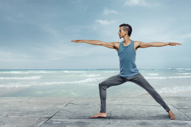 Young man doing yoga at the sea beach Young handsome man doing yoga at the sea beach warrior 2 stock pictures, royalty-free photos & images