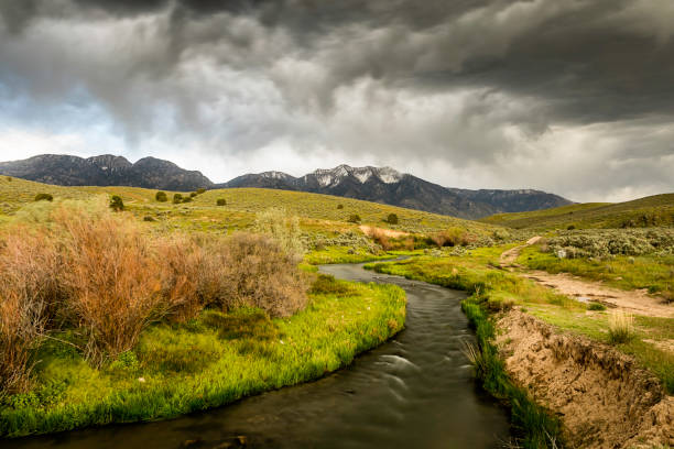 High quality landscape photo of a river in the Utah high desert with sagebrush and tall mountains in the distance.