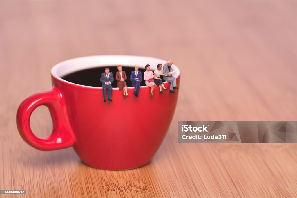 Concept créatif de boire du café et en attente. Les gens de la miniature s’assoient sur le bord d’une tasse de thé café pause-café. Tasse rouge sur un fond en bois. - Photo de De petite taille libre de droits
