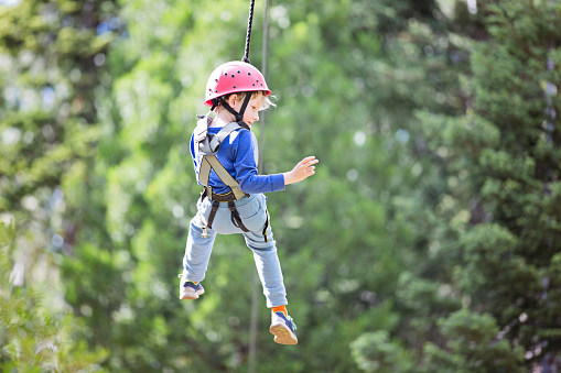 smiling little boy ziplining in treetop adventure park, healthy active lifestyle concept