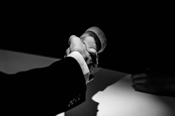 Anonymous business partners making handshake in shadow Black and white tone of anonymous business partners making handshake in dark shadow corruption stock pictures, royalty-free photos & images