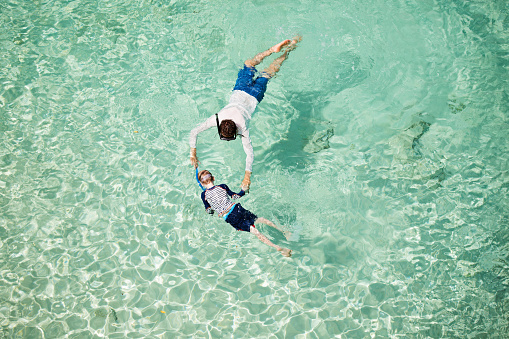 above aerial view of family of two, father and son, enjoying snorkeling in beautiful turquoise lagoon at anguilla island, caribbean, active family vacation concept