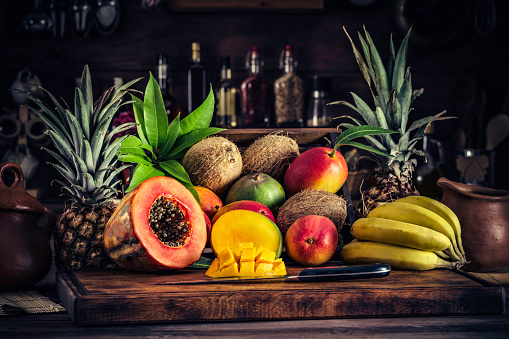 Wooden crates with assorted tropical fruits in rustic kitchen. Natural lighting. Mangos, pineapples, coconuts, bananas
