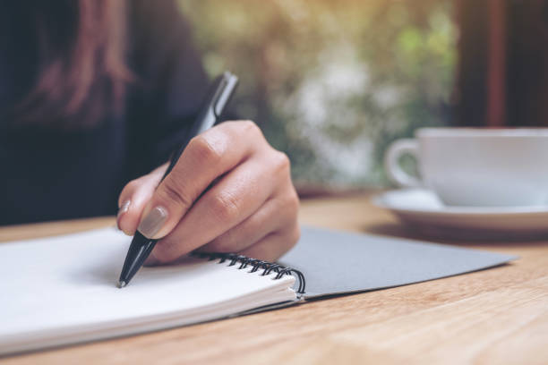 istock Closeup image of a woman's hand writing down on a white blank notebook with coffee cup on wooden table 1008161394