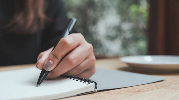istock Closeup image of a woman's hand writing down on a white blank notebook on wooden table 1008161396