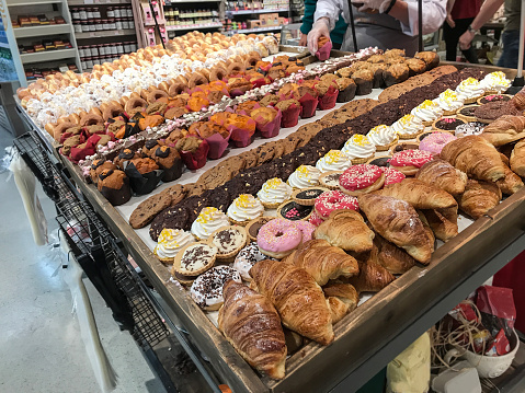 Display of various baked goods like cookies, tarts, muffins, donuts and croissants in the bakery section of a supermarket in a variety of colors