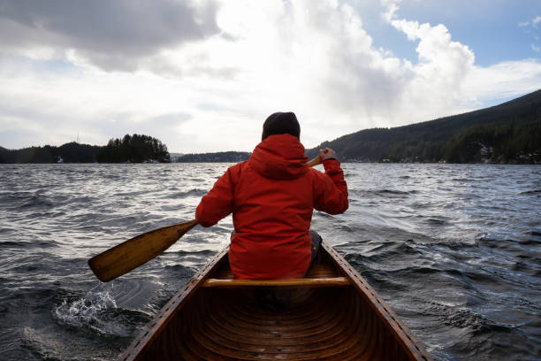 Man on a wooden canoe is paddling during a windy winter day. Taken in Indian Arm, North of Vancouver, British Columbia, Canada.