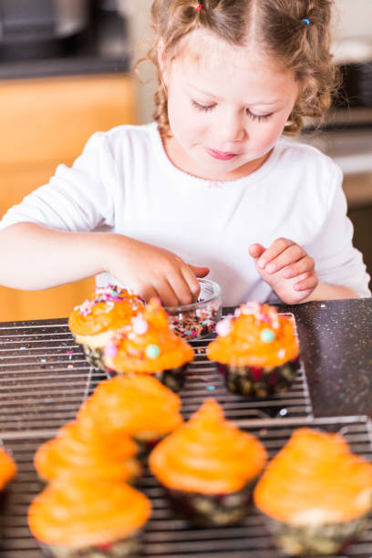 istock Little girl decorating orange icing on cupcakes with sprinkle mix. 1008177578