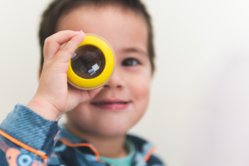 A 3-year old Eurasian boy is looking through a little yellow kaleidoscope at home