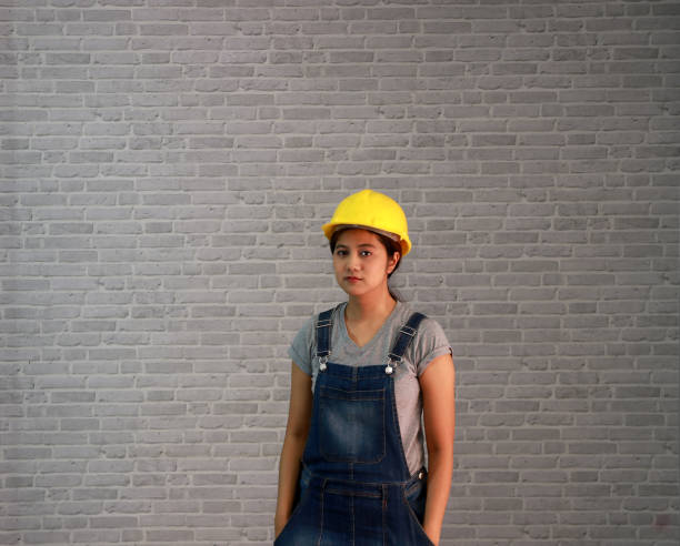 Technician woman ware yellow helmet with grey T-shirt and denim jeans apron dress standing and hands in pocket. stock photo