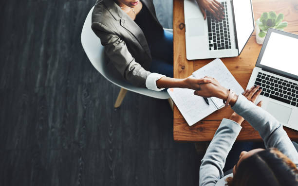 Let's merge our talents as we get to the top High angle shot of two businesswomen shaking hands in an office merger stock pictures, royalty-free photos & images