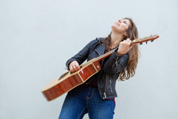 Happy inspired female guitarist performing song Happy inspired female guitarist performing song. Amazed young woman in leather jacket excited with playing guitar. Euphoria and street music concept singer back stock pictures, royalty-free photos & images