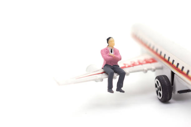 Miniature businessman sitting on airplane wing on white background
